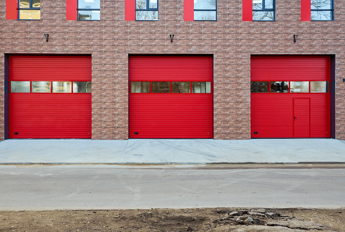 Three red garage doors on brick building.